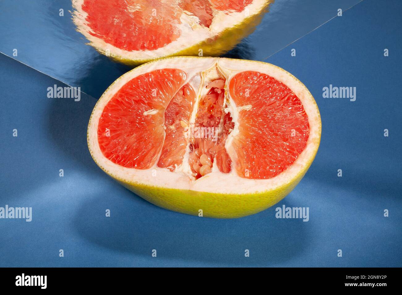 In Scheiben geschnittene, verspiegelte gelbe Grapefruit auf blauem Hintergrund Stockfoto