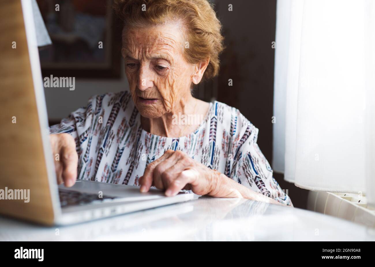 Ältere Frau mit kurzen Haaren mit Laptop zu Hause Stockfoto