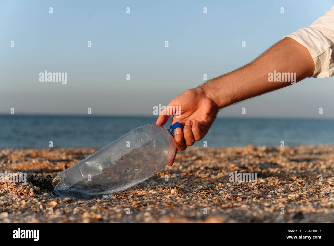 Mann pflückt Plastikflasche auf Sand am Strand Stockfoto