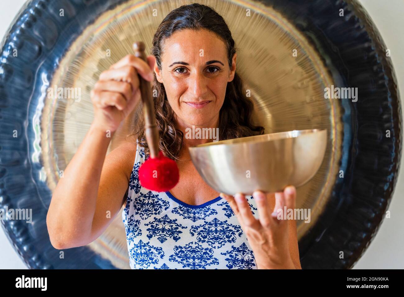 Lächelnde Klangtherapeutin mit Klangschale und Schlägel im Studio Stockfoto