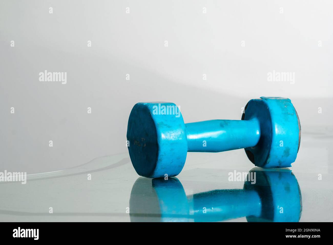 Blaue Kurzhantel (gebraucht, rostig) auf reflektierendem Glas und weißem Hintergrund, Platz für Text. Bewegungs- und Gesundheitskonzept. Fitnesskonzept Stockfoto