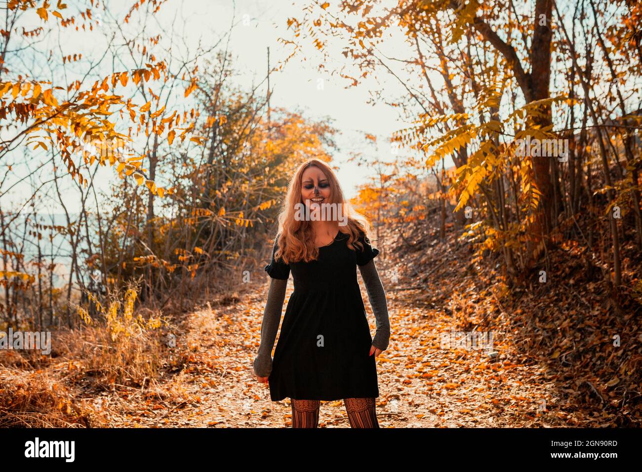 Lächelnde Frau mit Halloween Make-up steht im Herbst im Wald Stockfoto