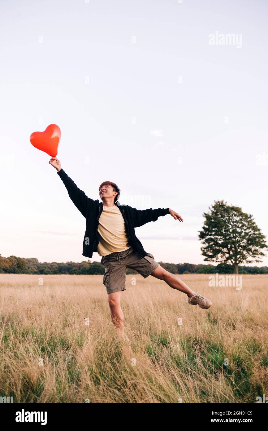 Junger Mann fängt einen Herzballon, während er auf der Wiese steht Stockfoto