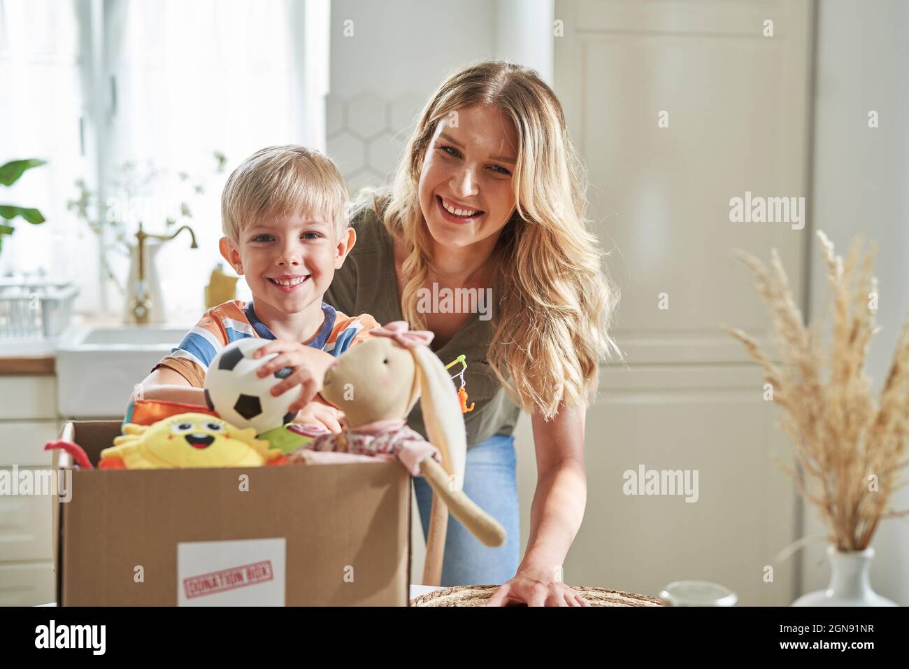 Lächelnde Frau und Junge stehen zu Hause an der Spendenbox Stockfoto