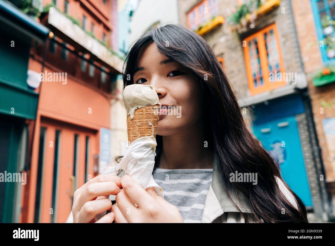 Junge Frau mit Eiskegel vor Gebäuden Stockfoto