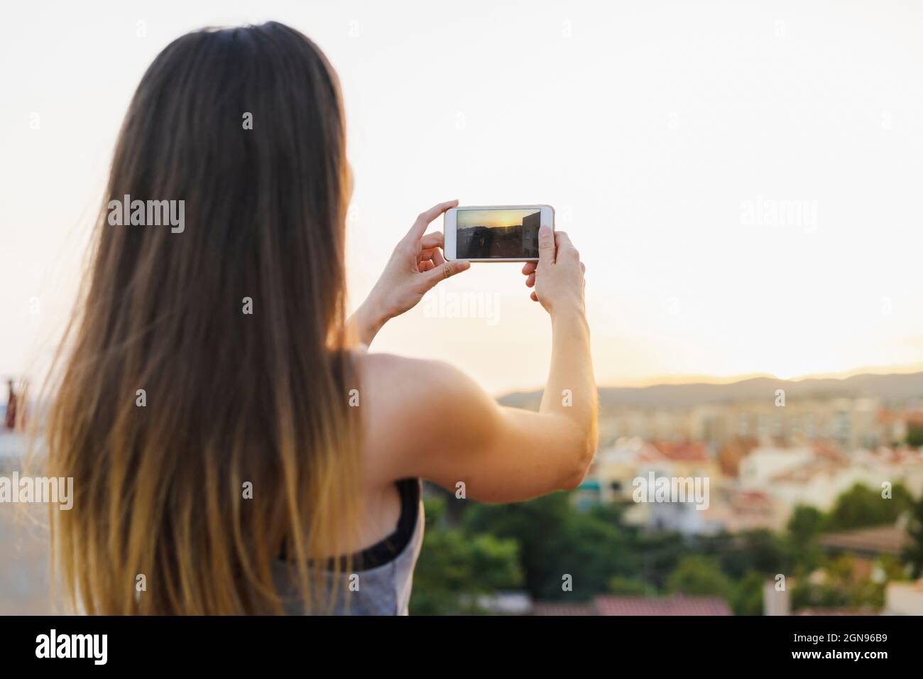 Frau, die den Sonnenuntergang über einem Smartphone auf dem Dach fotografiert Stockfoto