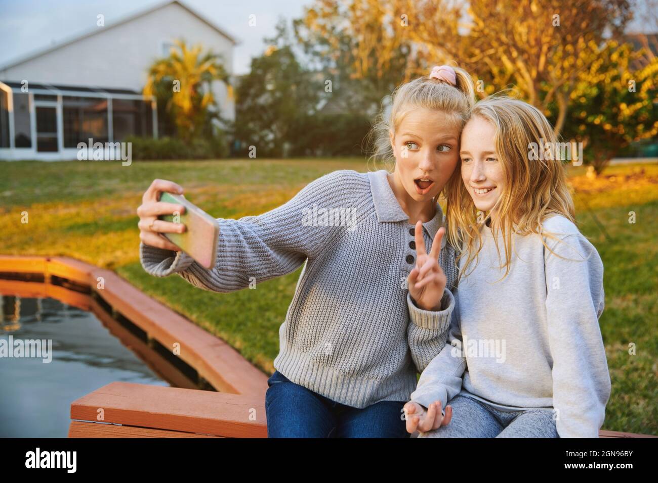 Mädchen mit offenem Mund gestikuliert, während Selfie mit Freund durch Smartphone am Teich Stockfoto