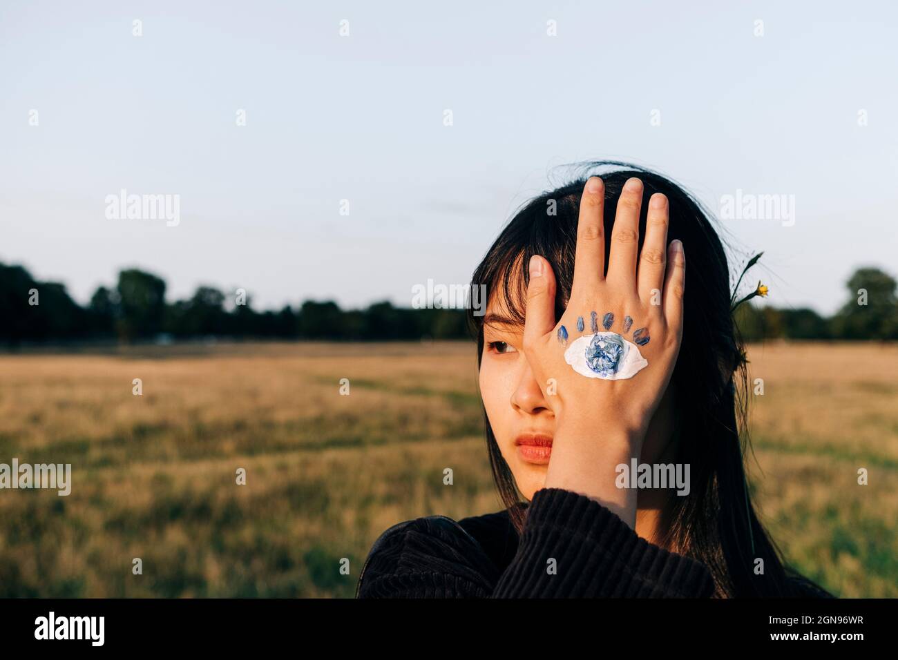 Junge Frau mit Farbe auf der Hand, die das Auge im Park bedeckt Stockfoto