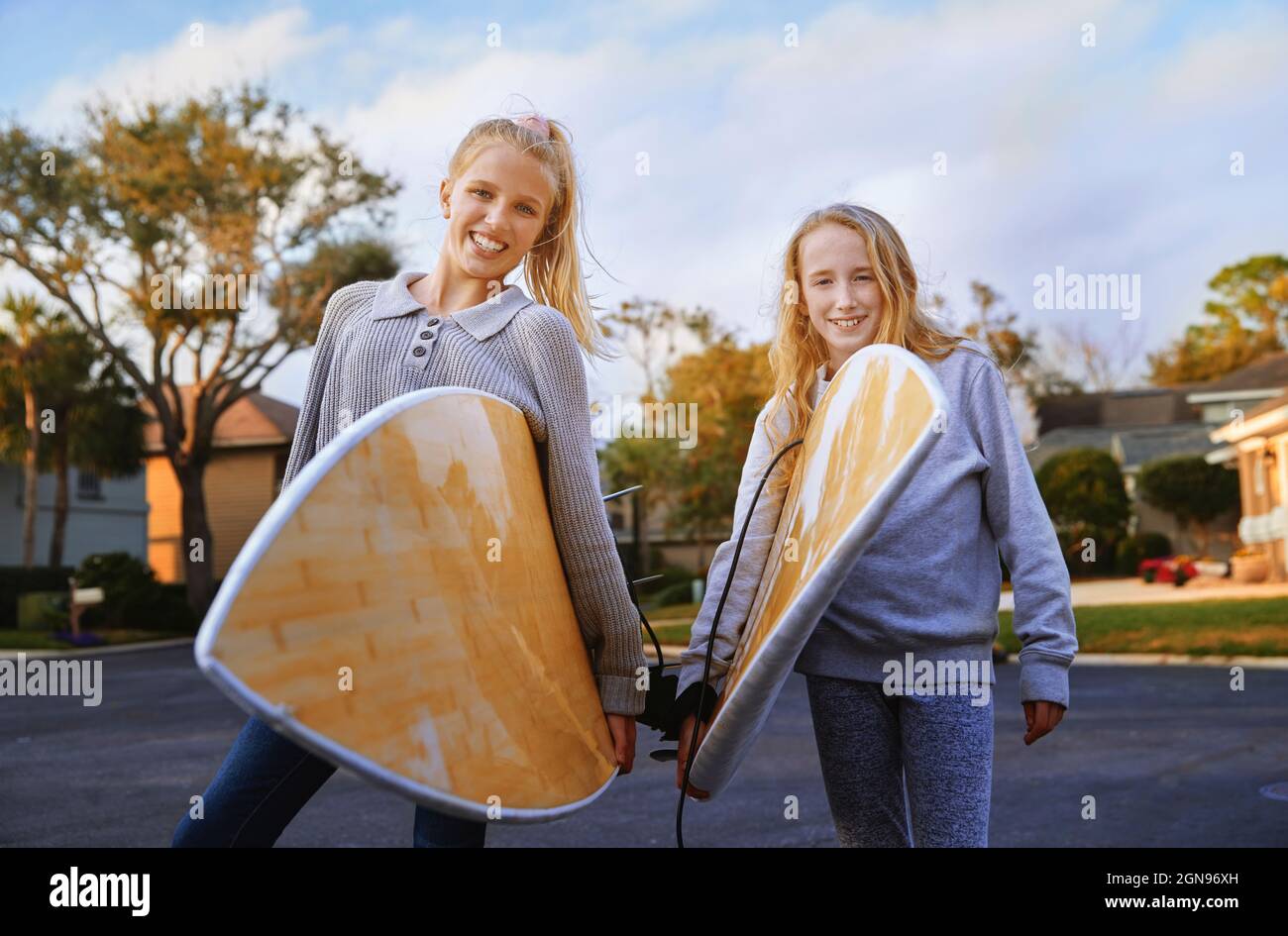 Lächelnde blonde Mädchen mit Surfbrettern, die auf der Straße stehen Stockfoto