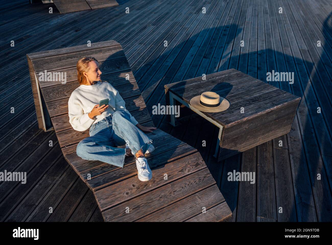 Frau mit Smartphone sitzt auf einer Holzbank Stockfoto