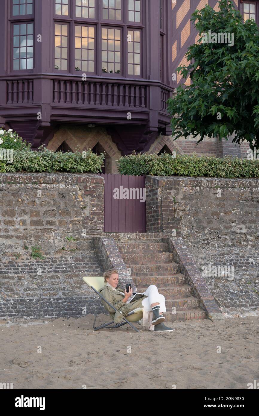 Eine Frau am Strand vor ihrer Villa schaute auf ihr Telefon Stockfoto
