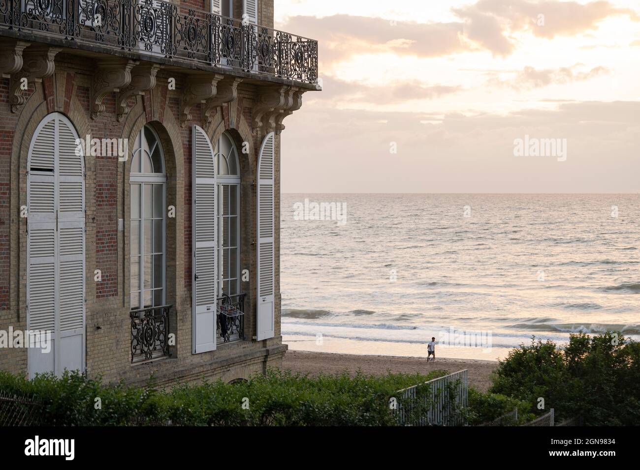 Luxuriöser Balkon mit Blick auf den Kanal bei Sonnenuntergang, ein Mann läuft am Strand Stockfoto