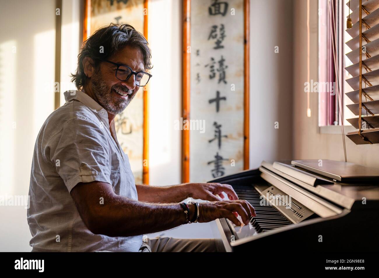 Lächelnder reifer Mann, der zu Hause Klavier spielt Stockfoto