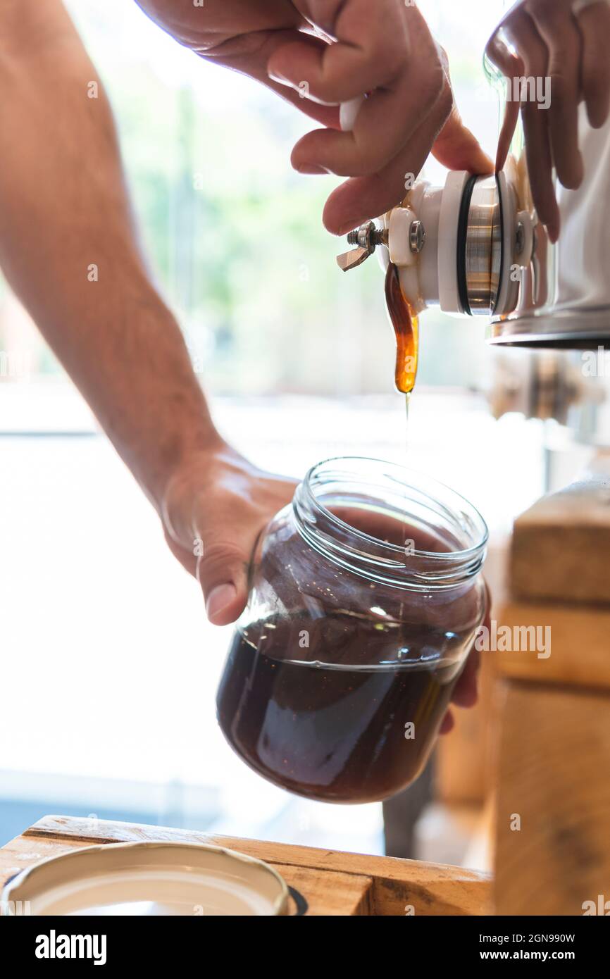 Männlicher Ladenbesitzer gießt Honig in ein Glas Stockfoto