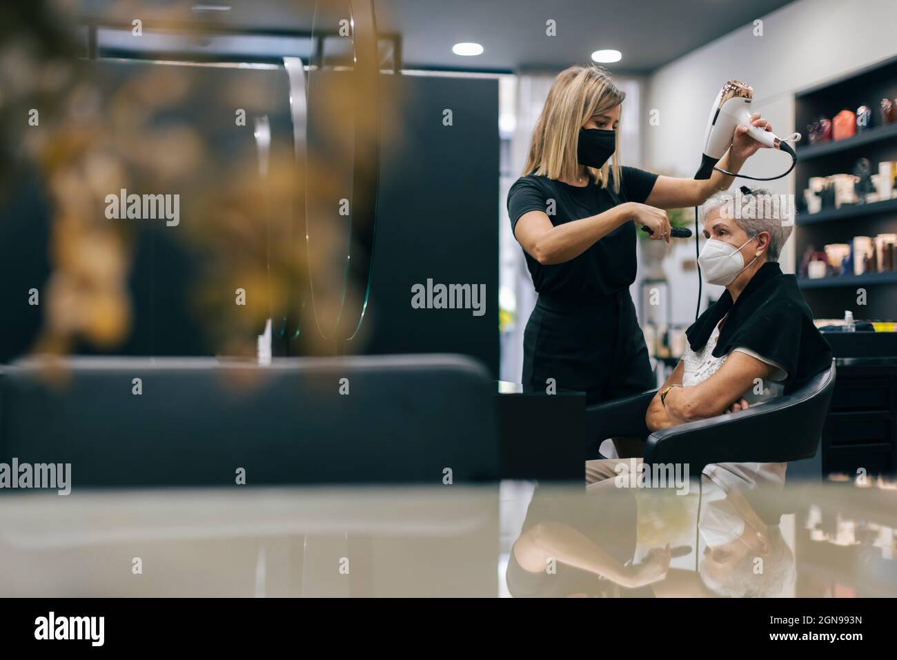 Weibliche Friseur mit Gesichtsmaske Schlag trocknende Kundenhaare im Salon Stockfoto