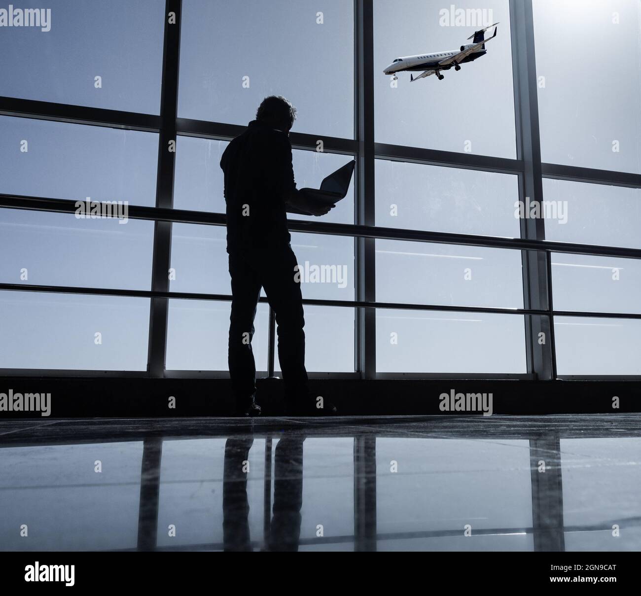 Mann mit Laptop im Flughafengebäude mit Privatjet im Hintergrund. Stockfoto