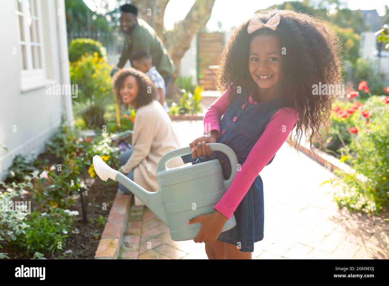 Glückliches afroamerikanisches Mädchen und ihre Familie gärtnern und gießen Pflanzen zusammen Stockfoto