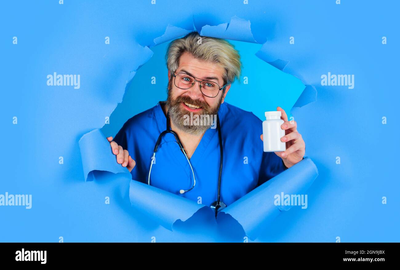 Arzt mit Pillen, die durch das Papierloch schauen. Pharmazeutisches Medikament. Männliche Krankenschwester mit Stethoskop mit einer Flasche Pillen. Apothekenkonzept. Stockfoto