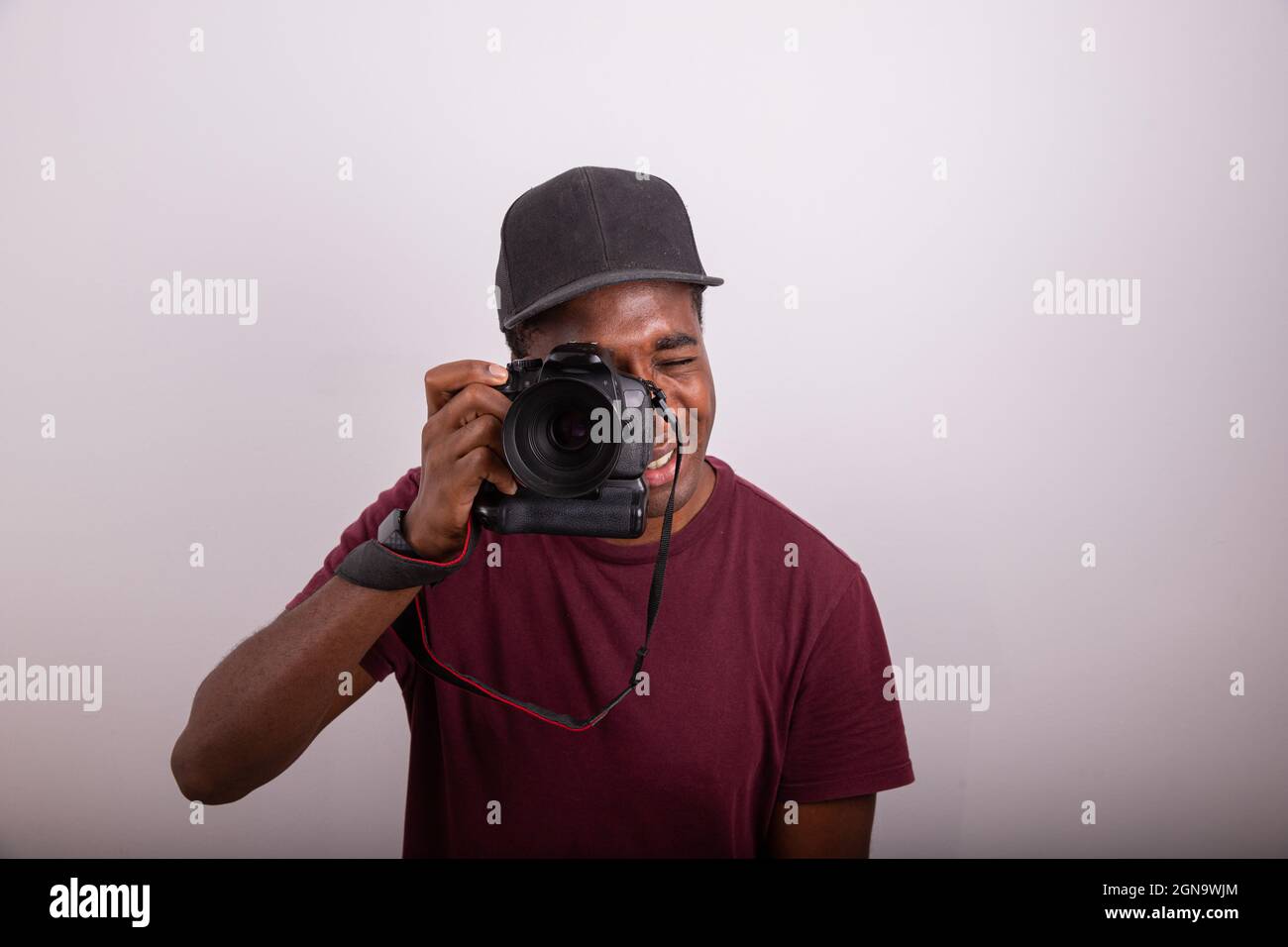 Der Fotograf nimmt ein Bild auf, während er durch den Sucher der Kamera schaut. Afrikanischer Fotograf isoliert auf weißem Hintergrund. Stockfoto