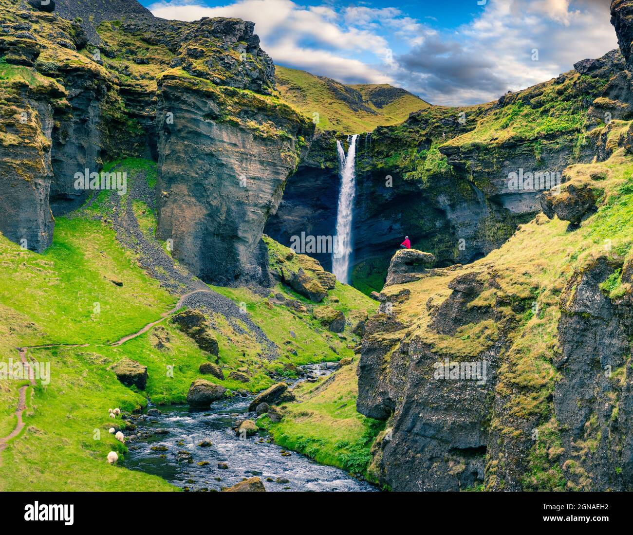 Farbenfrohe Morgenansicht des Kvernufoss Wasserfalls. Majestätische Szene in Südisland mit einem meditierenden Mann am Rande einer Klippe. Künstlerischer Stil nachbearbeitet Stockfoto