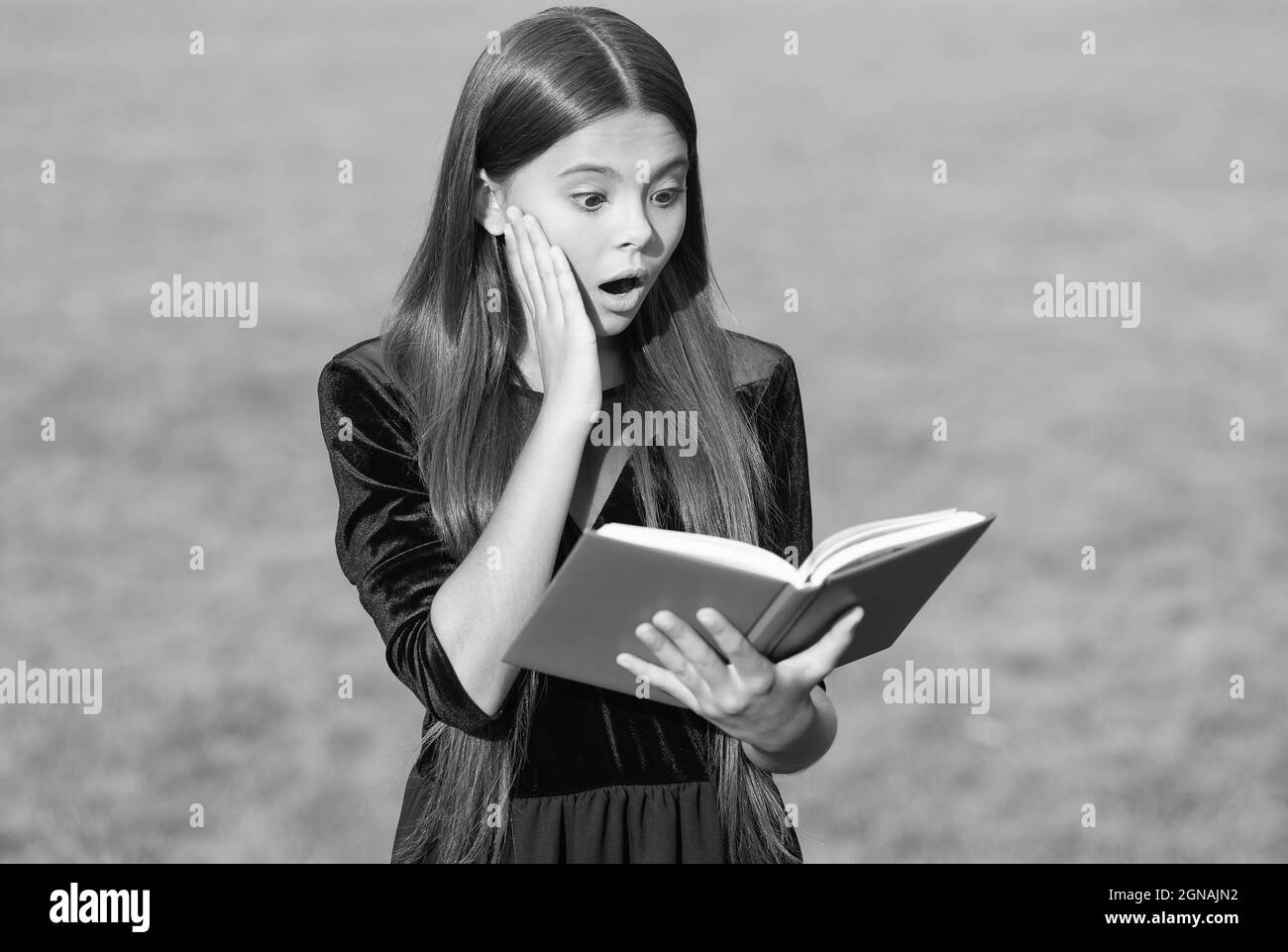 Überrascht kleines Kind mit offenem Mund lesen Schulbuch grünes Gras sonnigen Sommer im Freien, Informationen Stockfoto