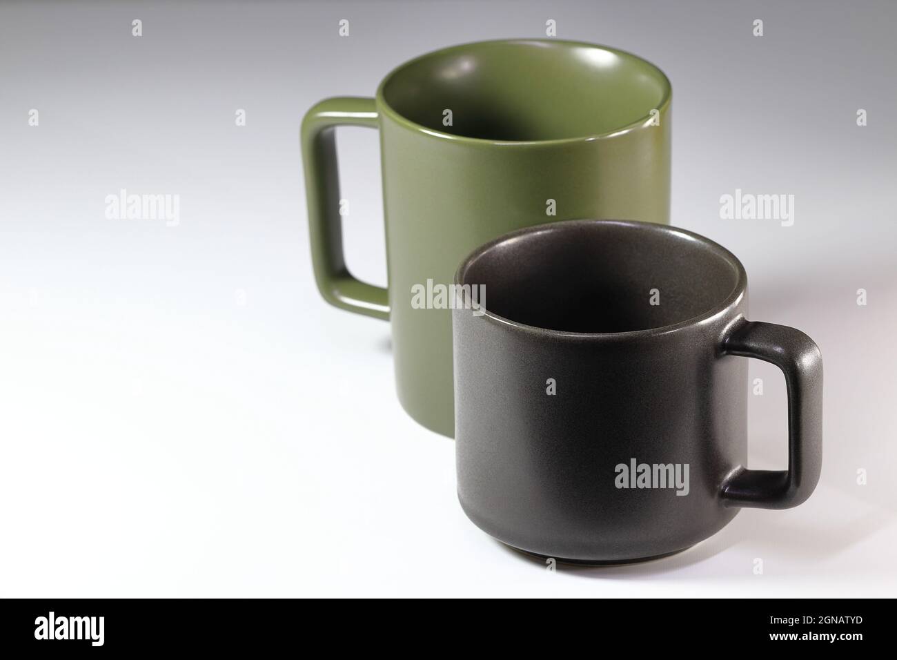 Nahaufnahme schwarzer und grüner Keramikbecher. Leere schwarze und grüne Tee- oder Kaffeetasse überlappen isoliert auf weißem Hintergrund. Stockfoto