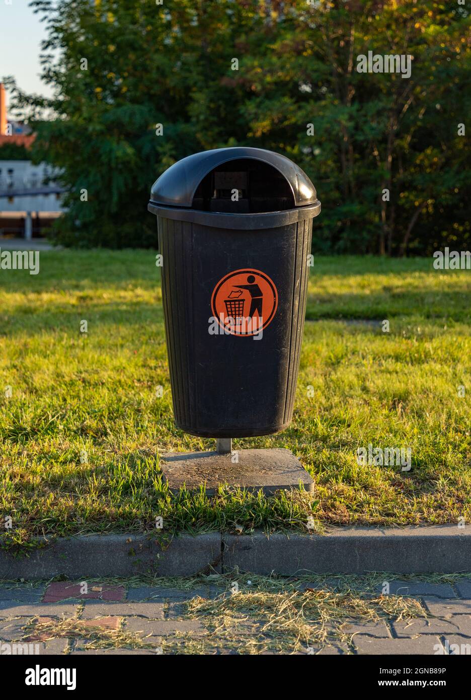 Ein Bild von einem Mülleimer an der Bordsteinkante eines Parkplatzes. Stockfoto