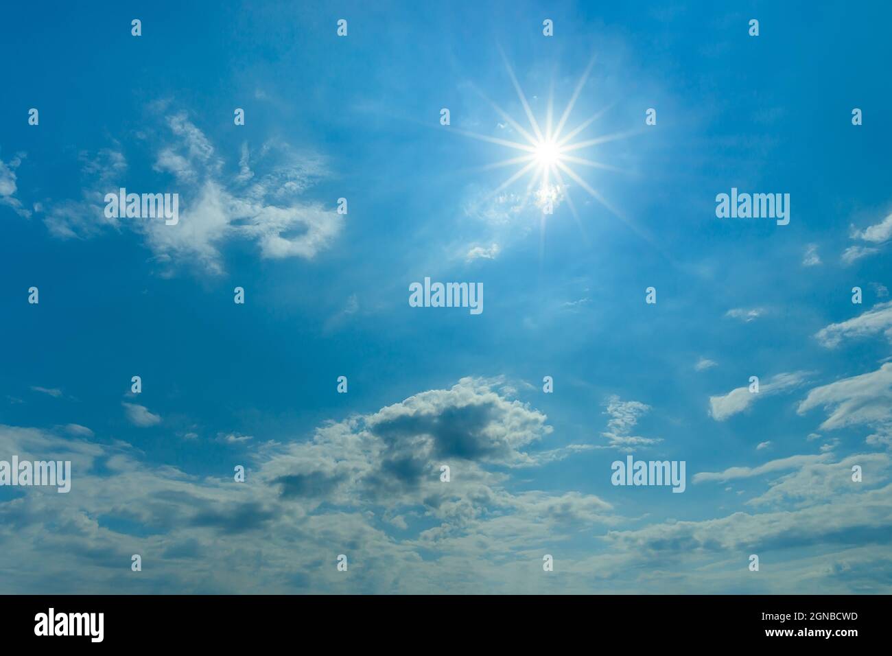 Die Mittagssonne scheint hell hoch am blauen Himmel. Blauer Himmel mit kleinen weißen Wolken an einem sonnigen Tag. Sonne am Himmel für Wettervorhersage Hintergrund. Stockfoto