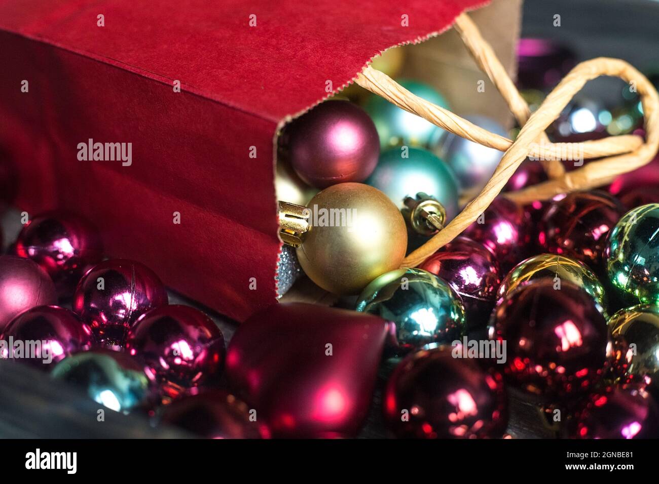 Kleine burgunderrote Geschenktasche mit bunten Weihnachtskugeln. Geschenke werden vorbereitet. Mehrfarbige Weihnachtsdekorationen für den kleinen Weihnachtsbaum. Postkartenbild Stockfoto
