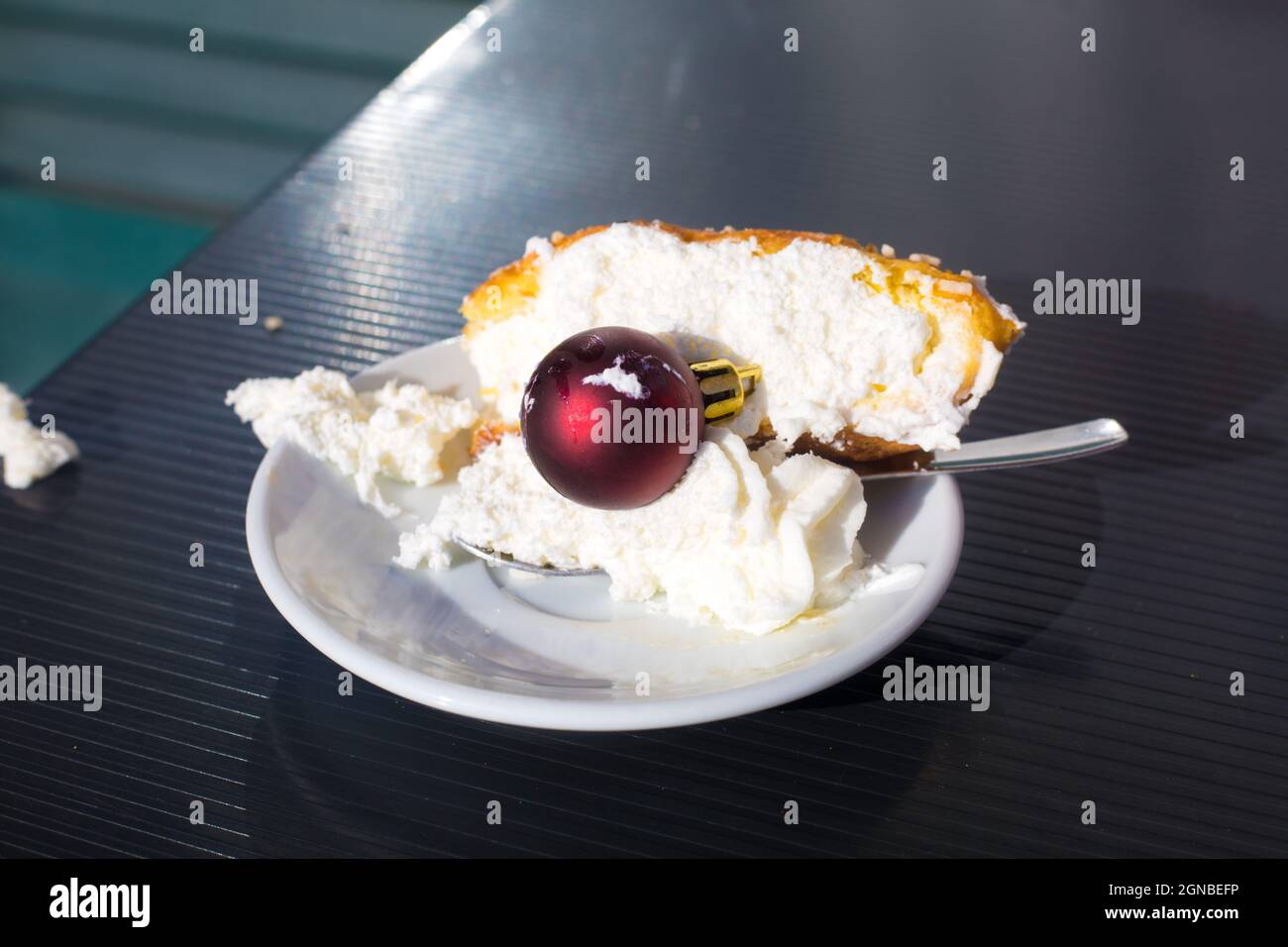 Nach Neujahr Party-Konzept. Am Morgen des 1. Januar. Stück Kuchen mit Schlagsahne auf weißem Teller mit Teelöffel und roter Weihnachtskugel darauf. Winter Stockfoto