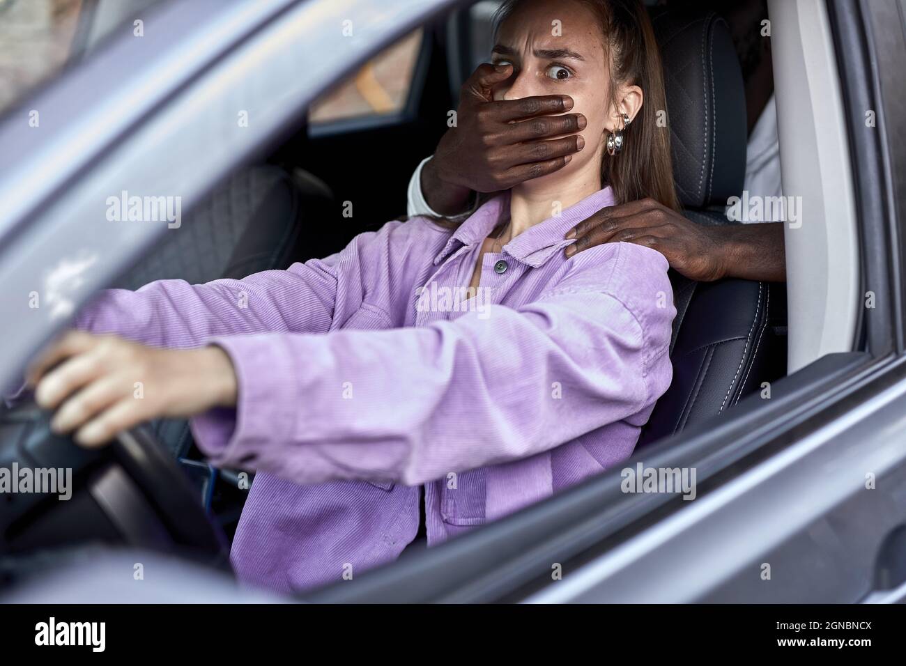 Gefährlicher schwarzer Mann, der verängstigte junge Frau im Auto bedroht, nicht erkennbarer afrikanischer Mann schließt den Mund einer verängstigten Frau und raubt. S Stockfoto