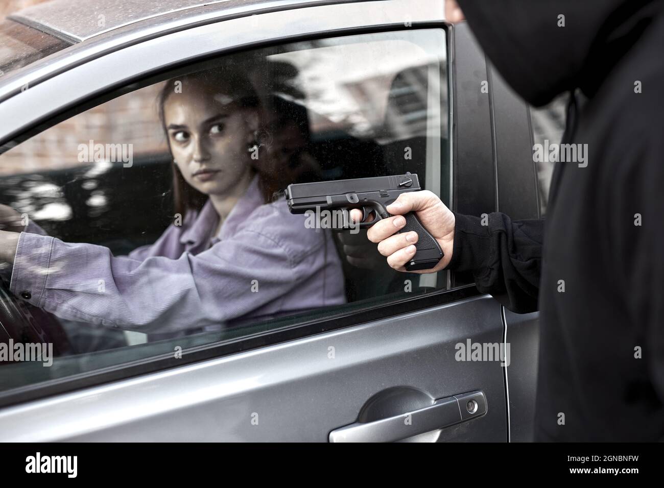 Bandit Mann Räuber hält Handfeuerwaffe Gangster zu entführen Geisel Frau Fahrer Auto schockiert und gefährlich auf Straße Gewalt Konzept. Seitenansicht auf sc Stockfoto