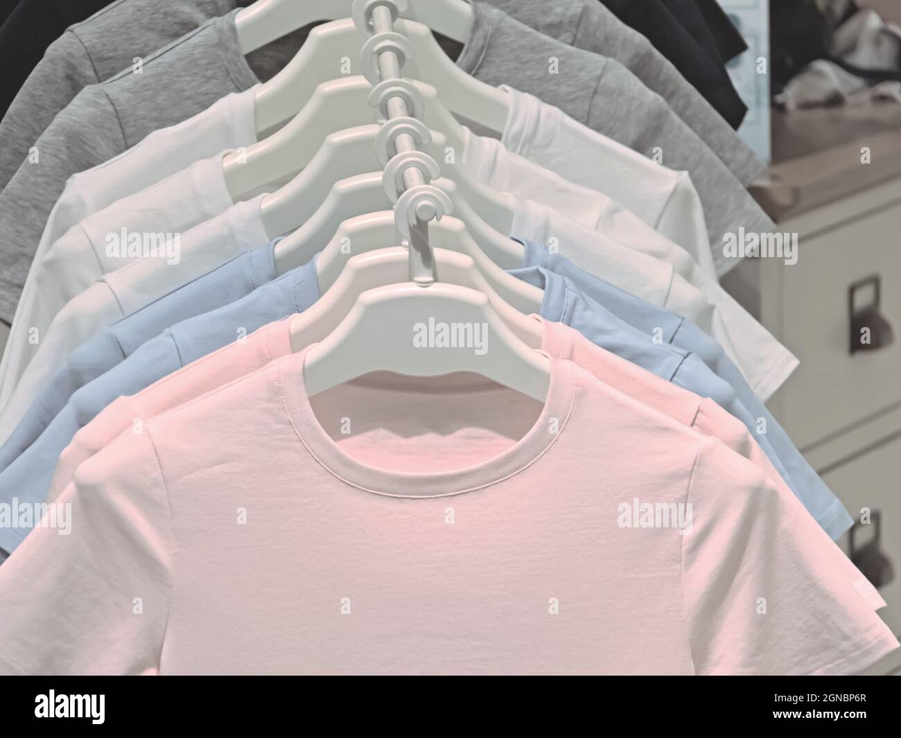 Helle T-Shirts hängen in einer Reihe an einem Kleiderbügel, Damenbekleidung aus Baumwolle Stockfoto