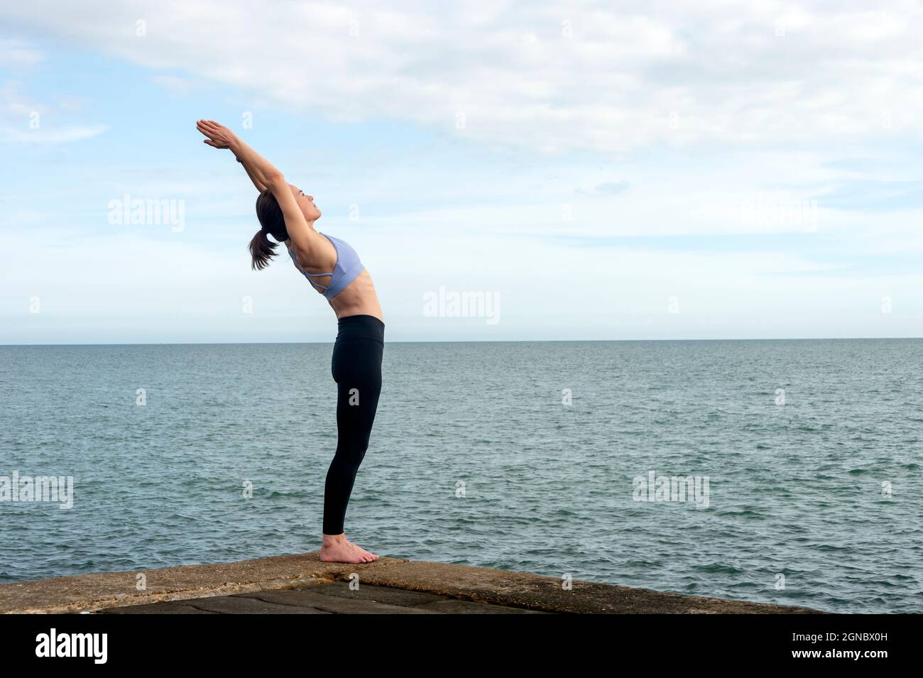 Yoga-Posen. Frau, die in der Hinterbeine Asana steht, übt in Anuvittasana Pose am Meer. Stockfoto