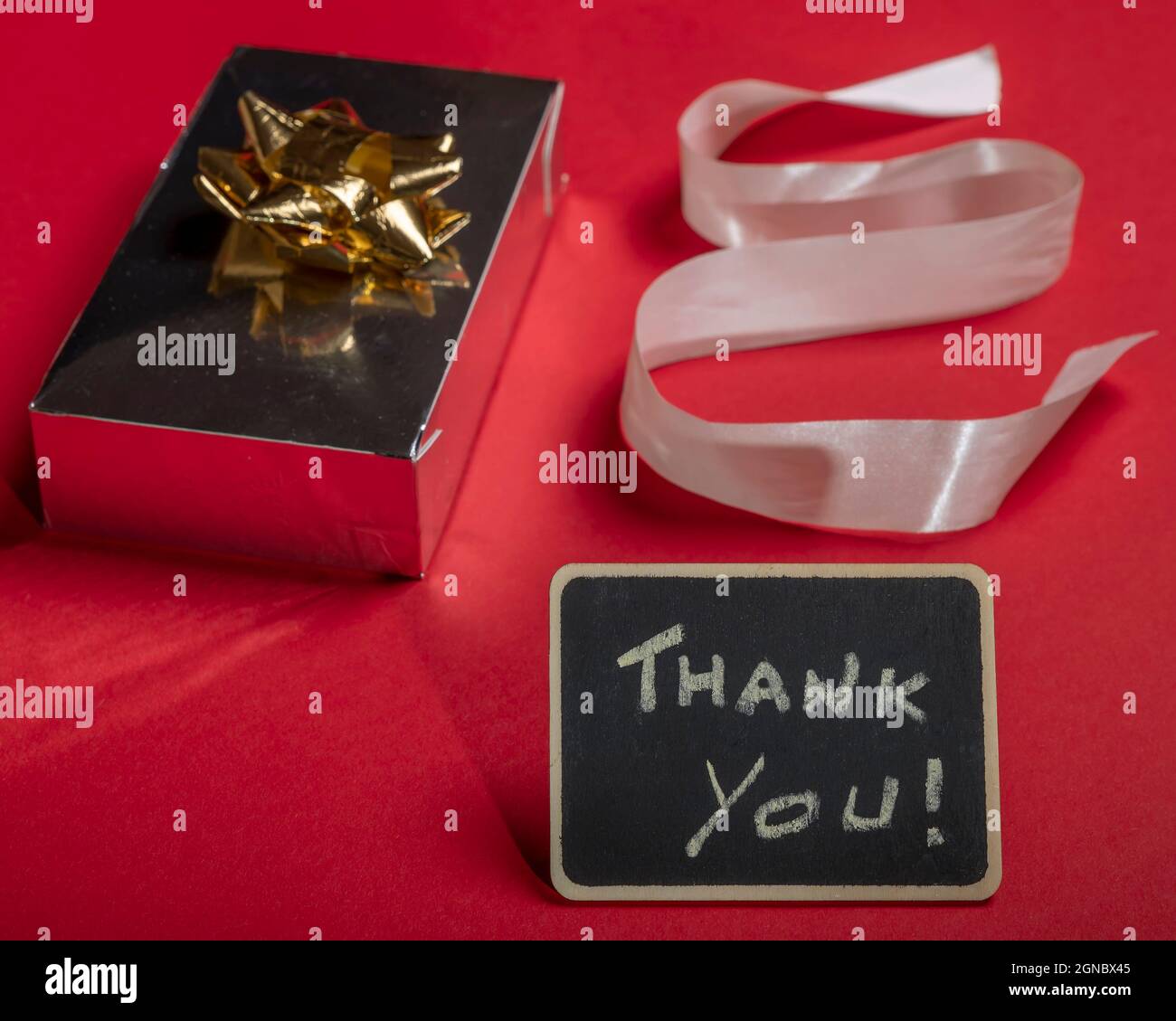 Komposition auf einem roten Hintergrund eines Geschenks mit Kakade, Band und Tafel mit den Worten „Danke!“ Stockfoto