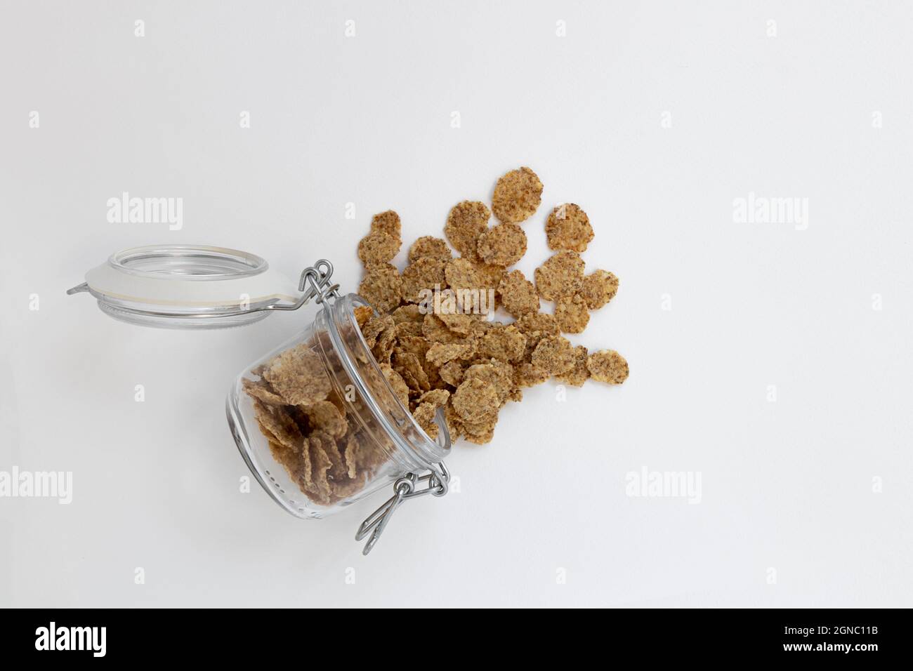 Glas mit offenem Deckel liegt auf weißem Hintergrund Vollkornflocken für gesundes Frühstück fallen aus Stockfoto