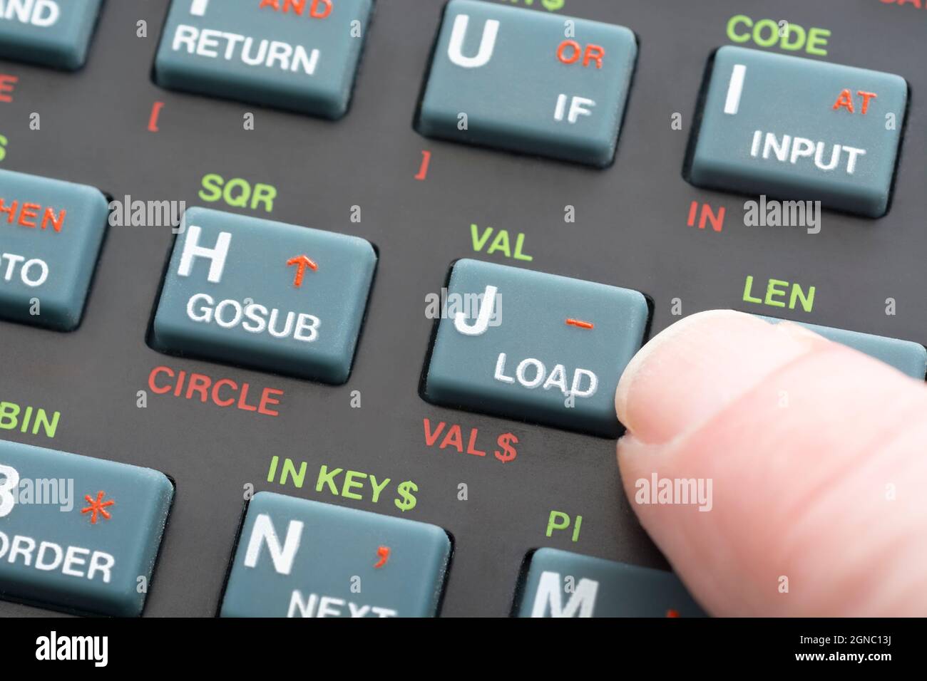 Nahaufnahme der Sinclair ZX Spectrum Tastatur. Fokus auf die Befehlstaste Basic LOAD Program mit Fingertipp. Klassischer 8-Bit-Heimcomputer aus den 1980er Jahren (siehe Hinweise). Stockfoto