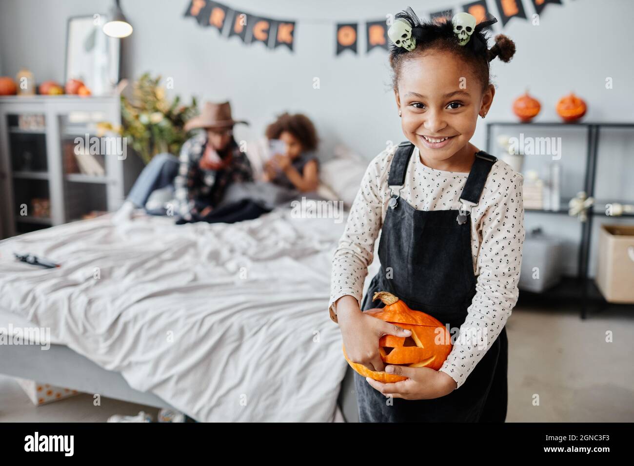 Waist-up-Porträt von glücklichen afroamerikanischen Mädchen gehalten geschnitzten Kürbis und lächelt an der Kamera, während im Zimmer mit Halloween-Dekorationen stehen, kopieren Raum Stockfoto