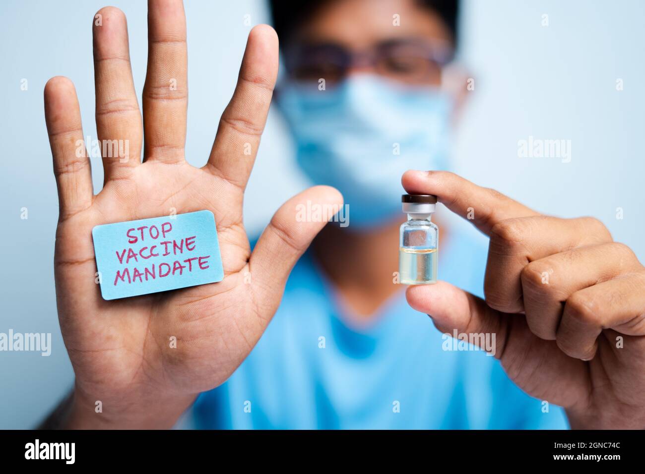 Fokus auf Hände, junger Mann mit medizinischer Gesichtsmaske, die das STOP-Impfmandat zeigt – Konzept-Impfzögerlichkeit. Stockfoto