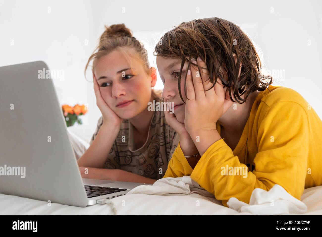 Kleiner Junge und Schwester im Teenageralter, die sich einen Laptop teilen und in einem Schlafzimmer zusehen Stockfoto