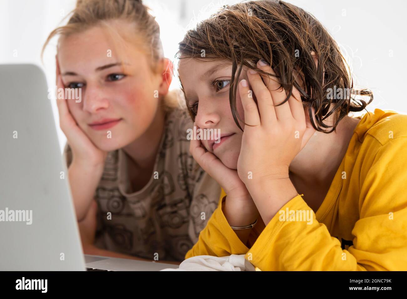 Kleiner Junge und Schwester im Teenageralter, die sich einen Laptop teilen und in einem Schlafzimmer zusehen Stockfoto