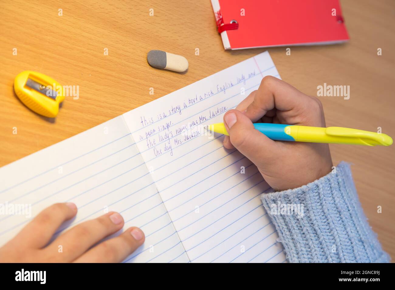 Die Hände von Nahaufnahme-Schülern schreiben auf Englisch in einem Notizbuch. Ein Schuljunge erledigt eine Aufgabe am Arbeitsplatz. Das Konzept der Kindererziehung, Vermittlung von Wissen, Fähigkeiten und Fähigkeiten. Stockfoto