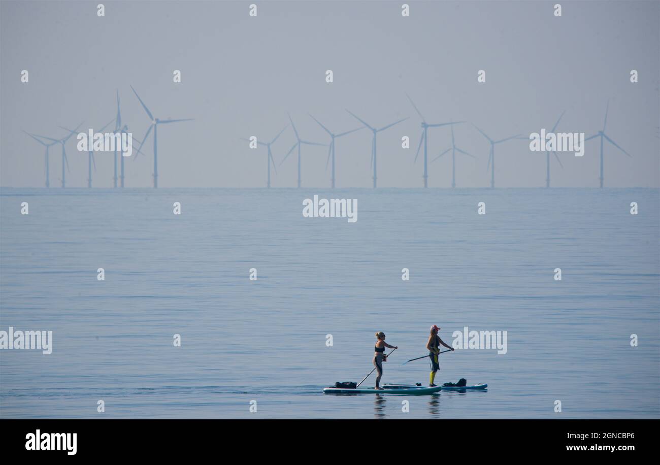 Paddelpärchen im Meer vor Brighton, East Sussex, England, mit der Rampion Windfarm am fernen Horizont. Stockfoto