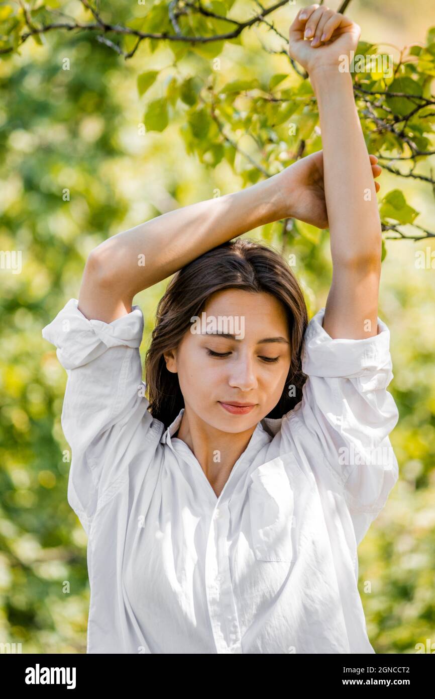 Ein Mädchen in einem weißen Hemd hob ihre Hände vor dem Hintergrund von Bäumen. Stockfoto
