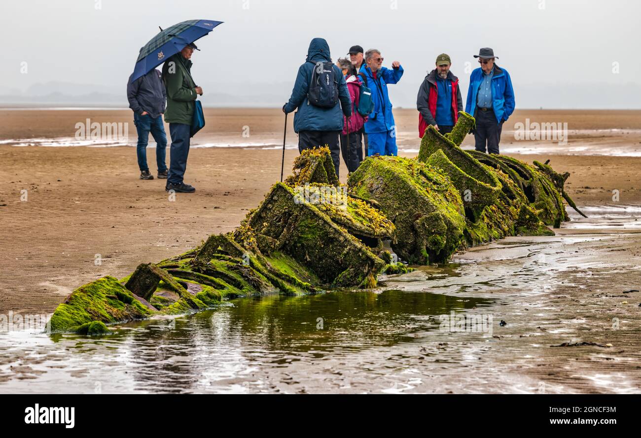 Gruppe von Wanderern, die das verfallene historische Wrack des Zwergsubmarinen der XT-Klasse des Zweiten Weltkriegs betrachten, das in Sand begraben ist, Aberlady Bay, East Lothian, Schottland, Großbritannien Stockfoto