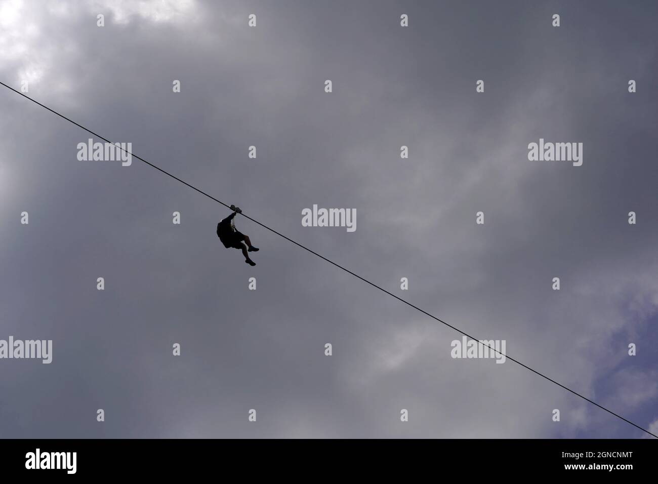 Seilrutsche oder Abseilen mit einem Mann in Silhouette. Auf dem Hintergrund befindet sich ein wolkiger Himmel sowie ein Kopierbereich. Stockfoto