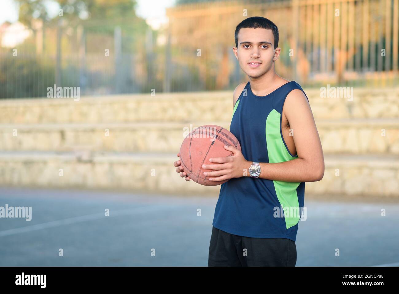 Kleines Kind mit Basketball. Fröhlicher Teenager mit Basketball auf dem Basketballplatz bei Sonnenuntergang. Stockfoto