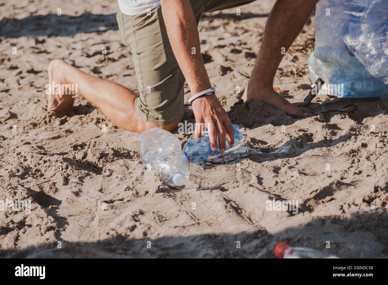 Junger Mann sammelt eine Plastikflasche und reinigt den Strand Freiwilligenkonzept. Kunststoff frei. Wir haben keinen Planeten B. Erde vor Plastik schützen Stockfoto