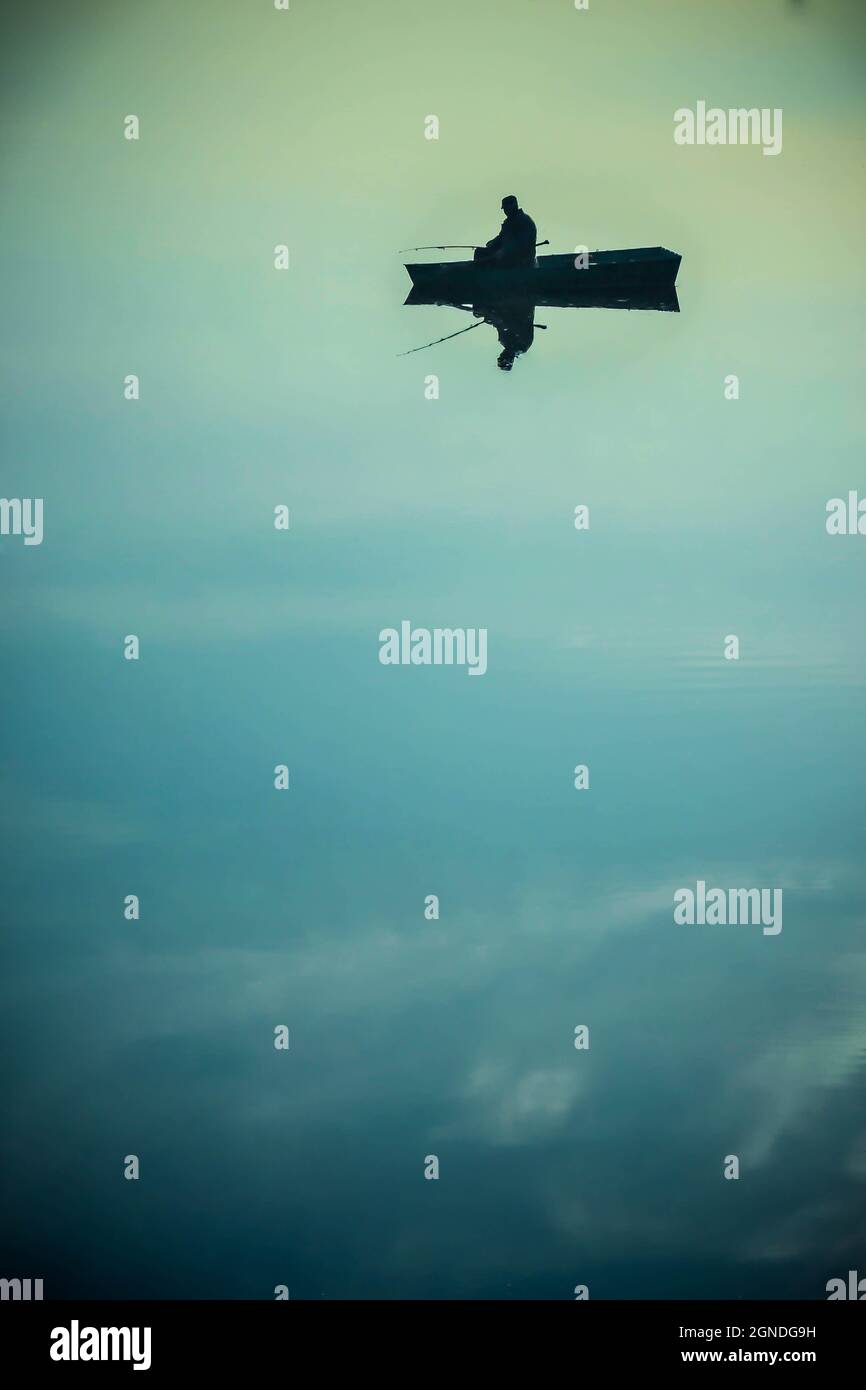 Schwarze Silhouette des Mannes in einem kleinen Boot auf dem See Stockfoto