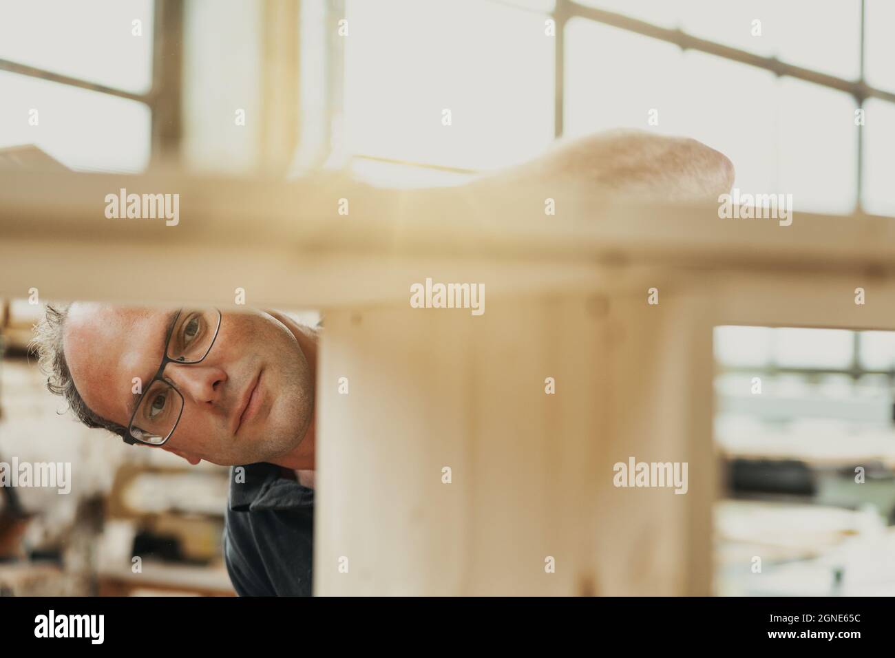 Zimmermann oder Tischler, der in einer Werkstatt an einem Holzschrank arbeitet oder unter den Rahmen schaut, um seine Verarbeitung zu überprüfen Stockfoto
